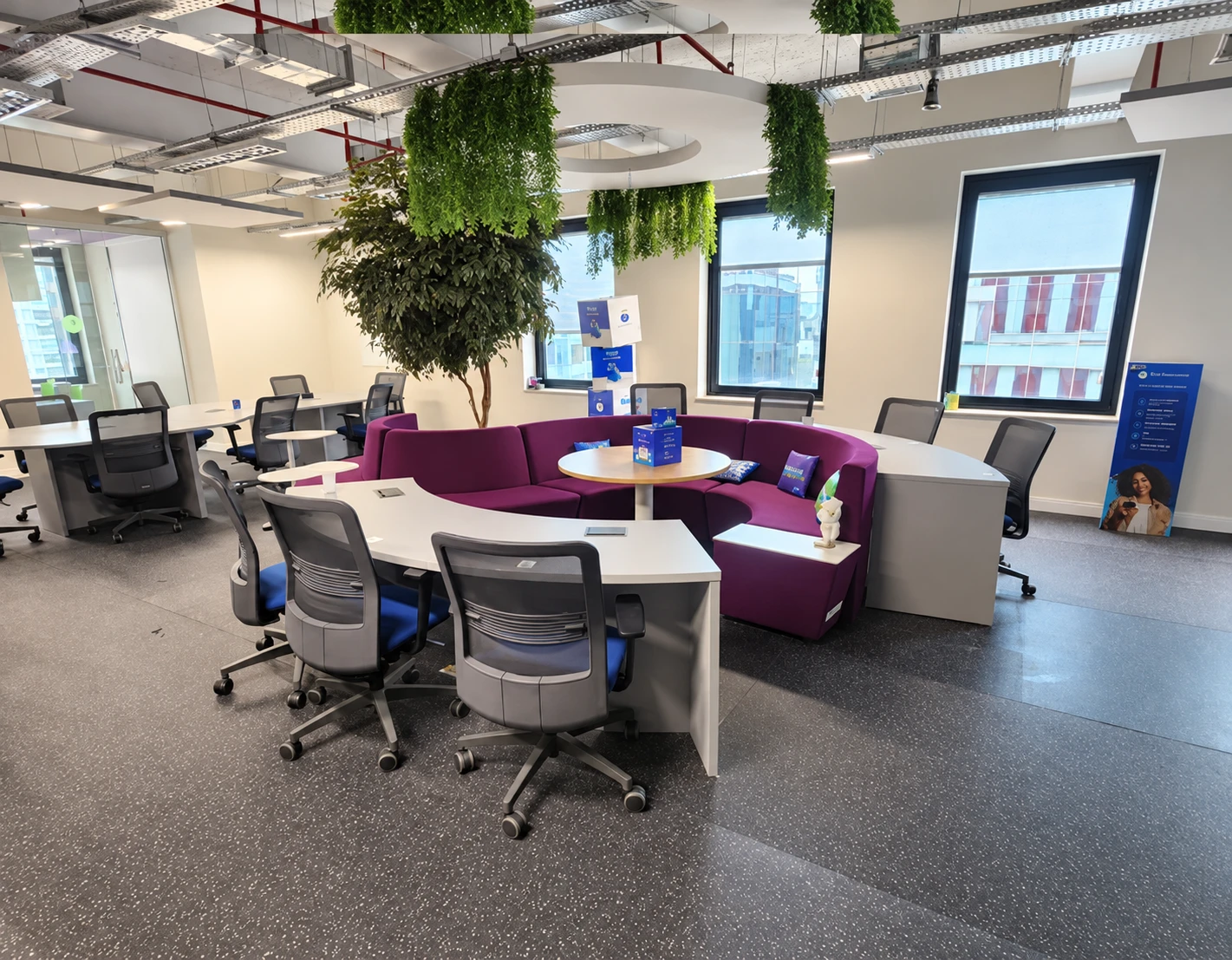 Espaço corporativo com sofá roxo, cadeiras e vegetação
