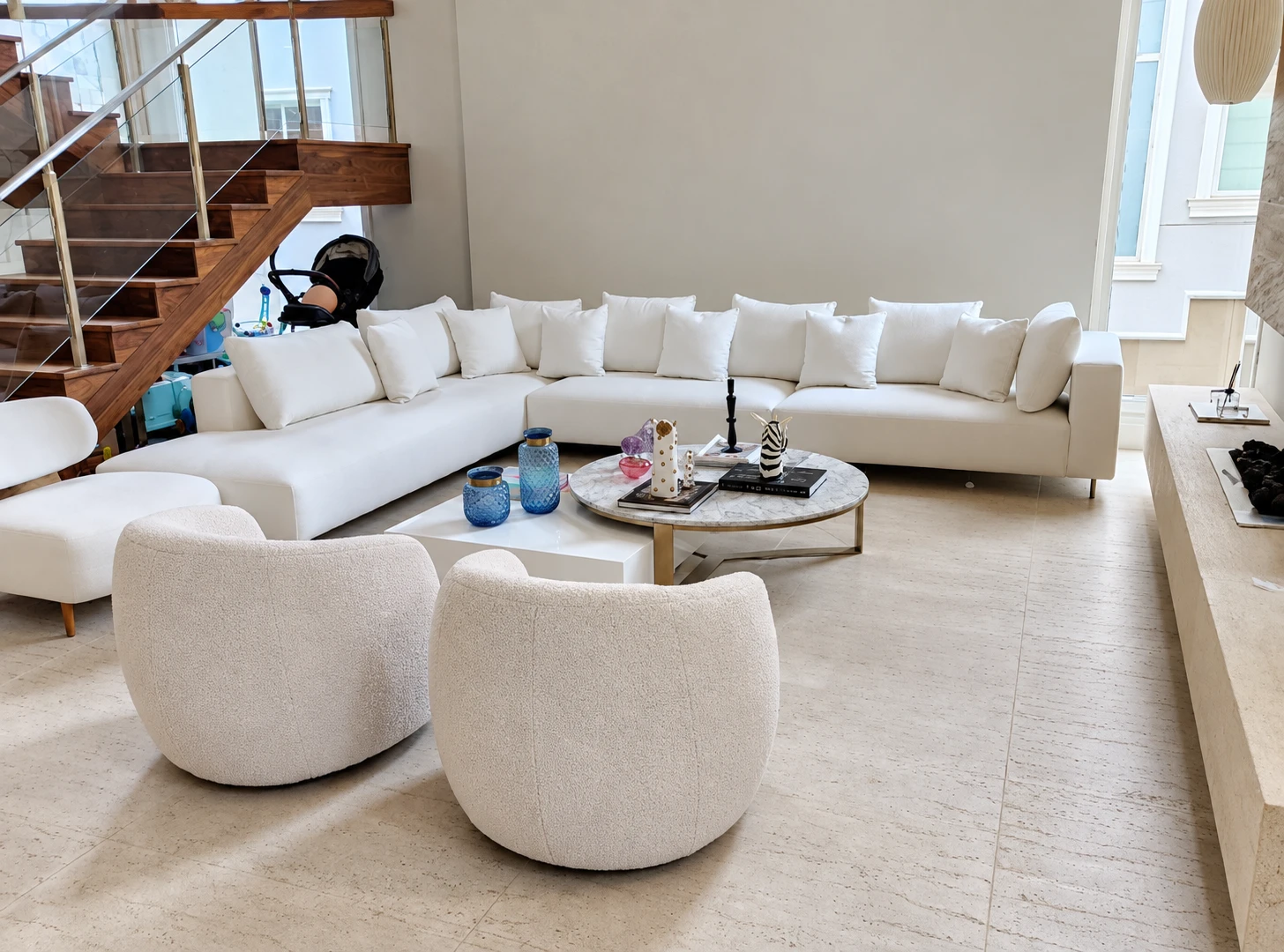 Sala clara com sofá em L, poltronas e escada de madeira